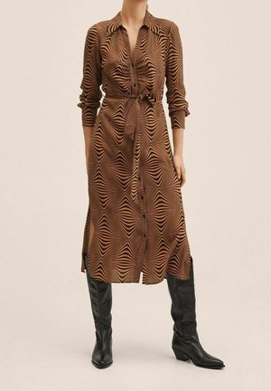 Robe chemise marron avec un motif en vagues dans des teintes d'orange, fermeture à boutons sur le devant, col, et taille cintrée. Porte avec des bottes noires jusqu'aux genoux.