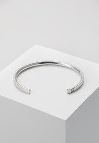 Sølvmetall armbånd med en glatt, avrundet design, med en åpen ende og stemplede merkinger på den ene siden.