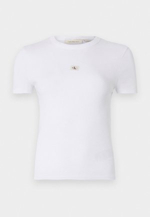 T-shirt bianco in cotone aderente con maniche corte, texture a coste e un piccolo patch con logo CK sul petto. Design minimalista.