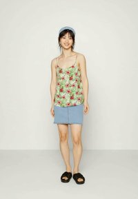 T-shirt de flores verdes com flores vermelhas, combinado com uma mini saia de denim azul claro. A modelo usa sandálias pretas de deslizar e uma faixa azul na cabeça.