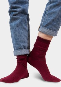 Burgundowe skarpetki w prążki, wykonane z miękkiego materiału, z dopasowanym fasonem w kostce. Połączone z podwiniętymi dżinsami.