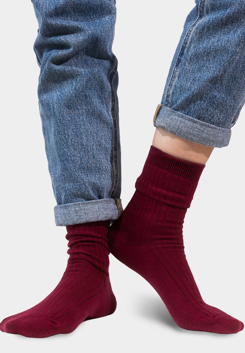 Burgundowe skarpetki w prążki, wykonane z miękkiego materiału, z dopasowanym fasonem w kostce. Połączone z podwiniętymi dżinsami.