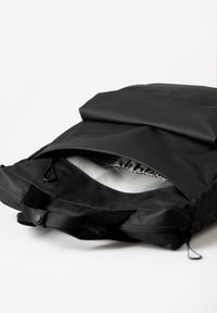 Zaino nero con un esterno texturizzato, dotato di chiusura a roll-top. L'interno è in tessuto grigio con tasche elasticizzate. Scomparto con zip in vista.