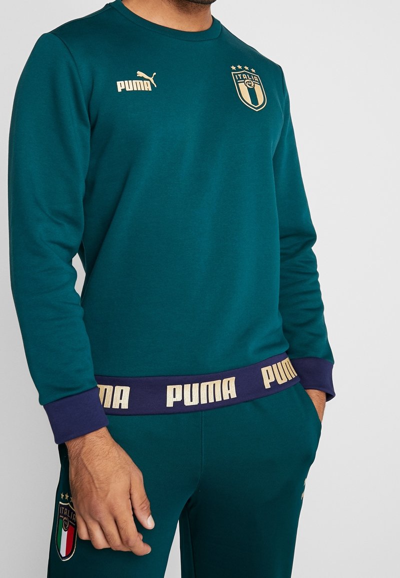 Tyrkysová mikina s dlouhým rukávem se zlatým logem Puma, italským znakem a fialovým pasem s nápisem "PUMA" ve zlaté barvě. Materiál z prodyšné směsi bavlny.