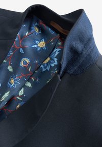 Námořnický blazer s kontrastní květinovou podšívkou, na které jsou modré, žluté a zelené květiny na tmavém pozadí, a texturovaným límcem.