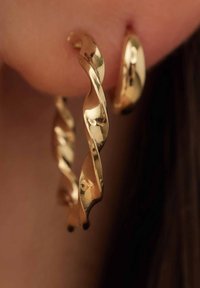 Boucles d'oreilles en or avec un design torsadé, surface réfléchissante et forme circulaire, suspendues au lobe de l'oreille avec des accents courbés.