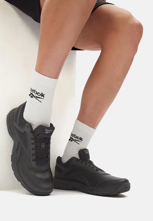 Czarne buty sportowe z gładką syntetyczną cholewką i teksturowaną gumową podeszwą, zestawione z białymi prążkowanymi skarpetkami z czarnym logo.