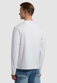 T-shirt bianco a maniche lunghe con scollatura rotonda, tessuto morbido e vestibilità comoda, abbinato a jeans di denim azzurri con accenti grafici.