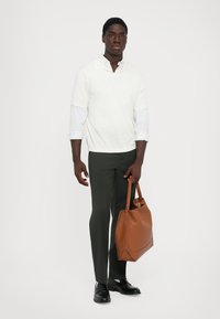 Hvit langermet skjorte lagd over en lys blå skjorte med krage, mørkegrønne bukser, svarte sko og en brun lær tote bag.