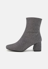 Grå ankelstøvler laget av strikkemateriale, med blokkheel, spiss tå, teksturert design og en tett passform rundt ankelen.