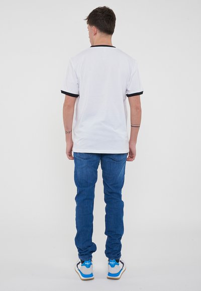 T-shirt bianca con bordi neri, abbinata a jeans blu. La maglietta ha una vestibilità comoda con maniche corte, dettagli minimi e una trama liscia.