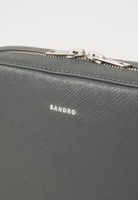 Pouch din piele texturată gri cu accesorii și fermoar din argint, având un logo embosat în alb.