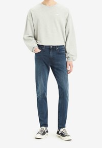 Gray sweatshirt with round neckline and loose fit, paired with dark blue jeans and black canvas sneakers with white soles.
