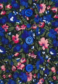 Modré knoflíky na látce s hustým květinovým vzorem, na kterém jsou růžové, modré a bílé květy a zelené listy na tmavém pozadí.