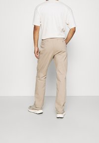 Beige broek met een rechte snit, voorzien van twee achterzakken en subtiele stiksels. Geloofd met een lichtgekleurde t-shirt en sneakers.