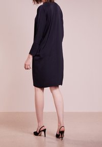 Knee-length mekko tummansinisestä sileästä kankaasta, jossa on pitkät hihat ja rento siluetti. Yhdistetty mustiin korkokenkiin.