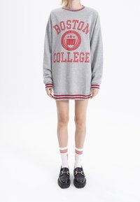 Šedá mikina s červeným nápisem "BOSTON COLLEGE" a emblémem. Má pruhované manžety a lem. Nosená s bílými ponožkami a černými platformovými botami.