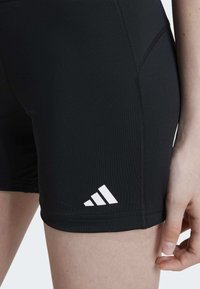 Čierne športové šortky s priliehavým strihom, vyrobené z hladkého materiálu, s bielym logom Adidas na dolnej ľavej strane.