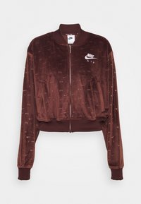 Hnědá sametová bomber bunda se zipem, žebrovanými manžetami a lemem. Obsahuje bílé vyšití loga Nike Air na levém prsu.