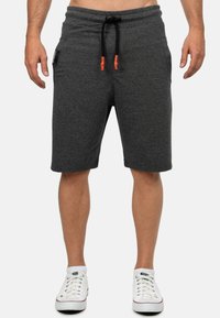 Grijze katoenen shorts met een verstelbare tailleband, voorzien van zwarte accentdrawstrings en twee zijzakken. De drager heeft witte schoenen aan.