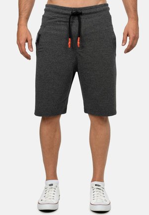 Shorts en coton gris avec une ceinture à cordon de serrage, présentant des accents de cordon noir et deux poches latérales. La personne porte des chaussures blanches.