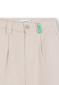 Beige hoge taille broeken met plooien. Voorzien van een knoopsluiting en een groene "SORRY" label op de tailleband. Zachte stofstructuur.
