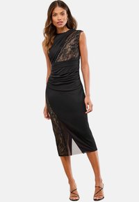 Abito nero con un design aderente, caratterizzato da dettagli in pizzo su una spalla e una fessura laterale, realizzato in tessuto liscio con dettagli drappeggiati.