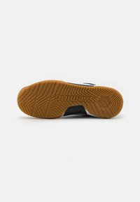 Zapatilla deportiva negra con una suela de goma texturizada, que presenta una suela de goma con un patrón de espiga y acentos blancos en los lados.