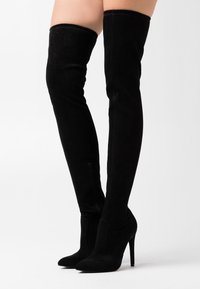 Lårhöga svarta mockastövlar med stiletto-klackar; formsydd design med sidodragkedja, mjuk textur och sömlös ovandel.