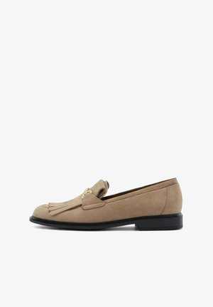 Beige suede instappers met een ronde neus, voorzien van een decoratieve franjerel en een goudkleurig accent; platte zwarte zool voor stabiliteit.