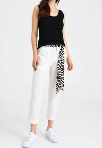 Czarny top bez rękawów połączony z białymi spodniami 7/8, z paskiem w zebrę. Model nosi białe sneakersy. Prosty, codzienny strój.