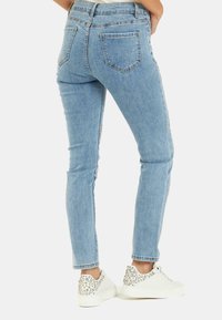 I jeans in denim blu chiaro presentano una vestibilità slim, cinque tasche e lati decorati con dettagli in argento. Indossati con sneaker bianche decorate.