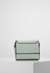 Mintgrøn crossbody taske med klaplukning, sorte accenter og en sølvfarvet kædetræ.