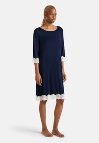 Abito blu navy con maniche 3/4, caratterizzato da dettagli in pizzo bianco all'orlo e ai polsini. Realizzato in tessuto morbido, design leggermente svasato.