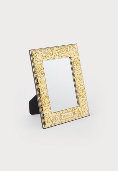 Ορθογώνιος καθρέφτης με ανάγλυφο χρυσό πλαίσιο που διαθέτει περίπλοκα λουλουδένια σχέδια, μαύρη βάση και λογότυπο Versace στο κάτω μέρος.
