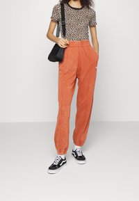 Top met luipaardprint en korte mouwen met zwarte afwerking; oranje joggingbroek met elastische boorden; zwarte crossbody tas; zwart-witte sneakers.