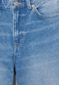Close-up van het voorste gedeelte van blauwe denim jeans met een metalen knoop, ceintuurlus, voorzak en oranje stikdetails.