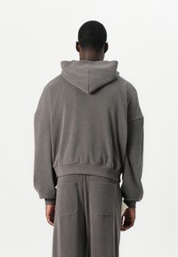 Grauer Hoodie aus strukturiertem Material mit lockerer Passform, übergroßen Ärmeln, Kängurutaschen und einer Kapuze.