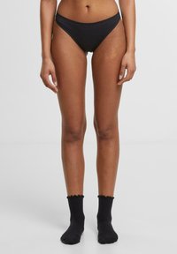 Fekete pamut bikini alsó, alacsony derékú kivitelben. A modellen fekete bordázott bokazokni van, fodros tetejével.