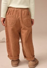 Pantaloni in corduroy marrone con vita elasticizzata, orli arrotolati e due tasche posteriori. Il tessuto ha una finitura strutturata.
