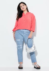 Felpa corallo con cappuccio e tre bottoni, abbinata a pantaloni leggeri blu chiaro con stampa e borsa metallica argento. Sandali neri con zeppa dotati di fibbia.