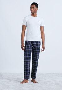 Bílé bavlněné tričko a tmavě modré kostkované pyžamové kalhoty. Kalhoty mají modré a světle šedé linky na tmavém pozadí. Žádné boty nejsou na nohách.