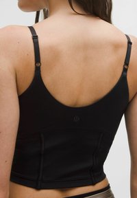 Prim-plan al spatelui unei femei care poartă un top sport negru fără mâneci, cu bretele ajustabile și un mic logo în centrul acestuia.