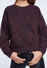 Sweatshirt a righe zebrate marrone e nera con maniche lunghe e scollatura rotonda. Tessuto morbido con vestibilità comoda e motivi dettagliati.