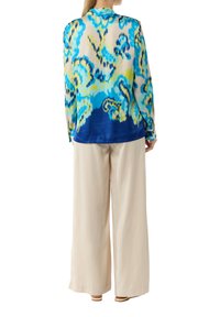 Langsleeve, blauw-groen patroon blouse met een semi-doorzichtige textuur, gecombineerd met losse crèmekleurige broeken en platte sandalen.