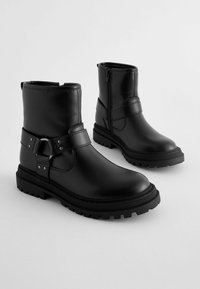 Schwarze Leder-Stiefeletten mit flacher Sohle, runder Zehenpartie, einem Riemen mit metallischem Akzent und seitlichem Reißverschluss für ein einfaches An- und Ausziehen.