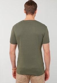 Olivově zelené tričko s krátkým rukávem, kulatý výstřih, hladká textura, přiléhavý střih, jednoduchý design; viditelné švy podél lemu a rukávů.
