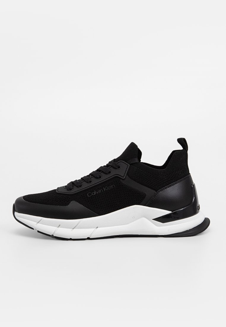 Baskets noires avec une tige en mesh respirant, des accents en cuir synthétique, une semelle intermédiaire blanche et une semelle texturée. Nom de la marque affiché en évidence.