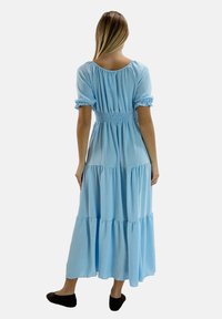 Lys blå tiered maxi kjole med smocked talje, korte puff�ærmer og blødt, flydende stof. Barfodet med sorte slip-on sko.