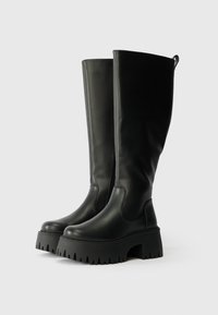 Crne čizme do koljena od glatke kože s debelim platformama, s bočnim zatvaračem i teksturiranim uzorkom na potplatu.